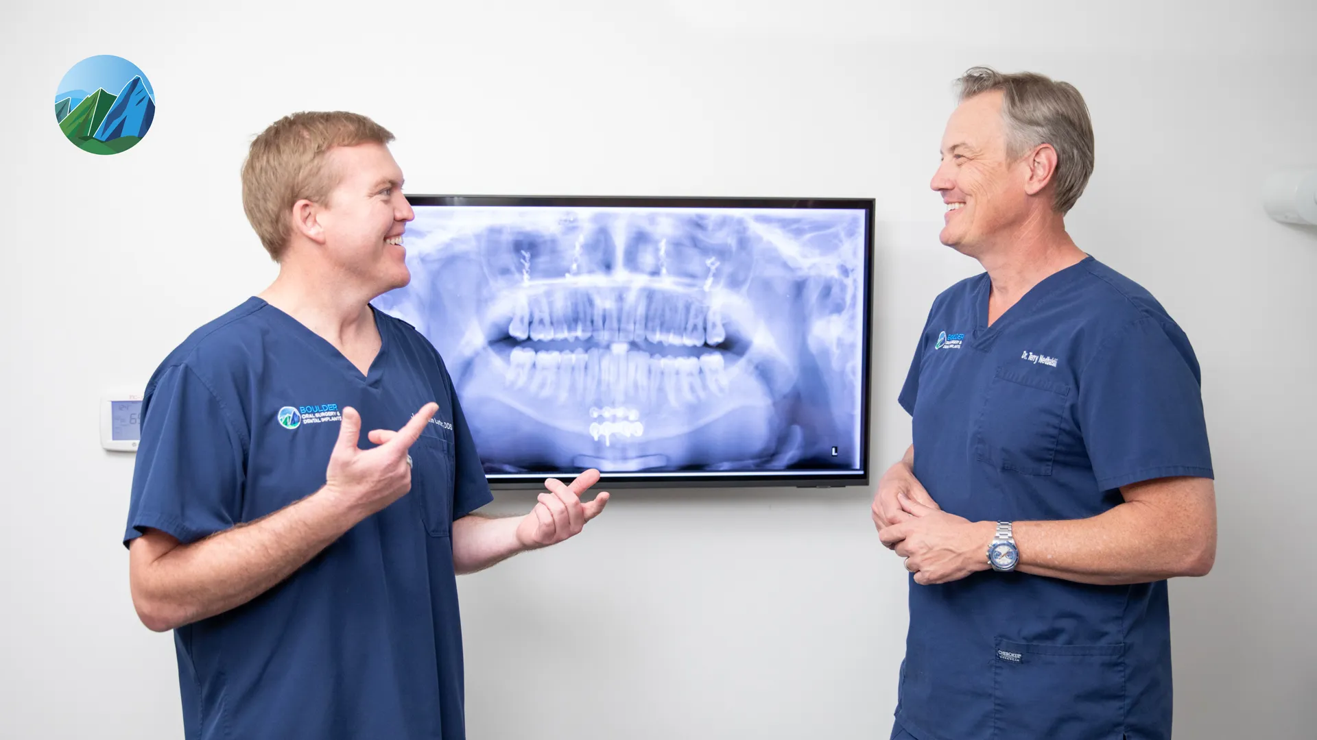 Two oral surgeons in navy scrubs discussing a panoramic dental X-ray on a screen